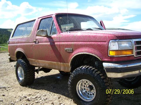1995 Ford Bronco - This lifted 1995 Ford Bronco is shown in a rural setting with a bright blue sky overhead.