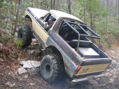 1992 Ford Mustang - Off-road pickup truck with custom roll cage and oversized tires tackling a challenging rocky terrain.