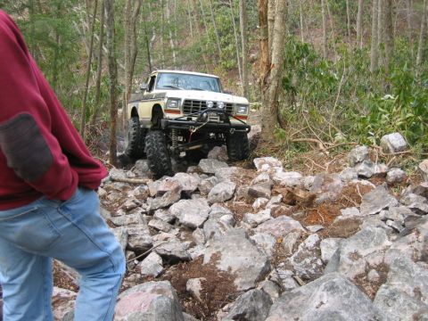 1992 Ford Mustang - A modified pickup truck navigates a rocky off-road path surrounded by trees.