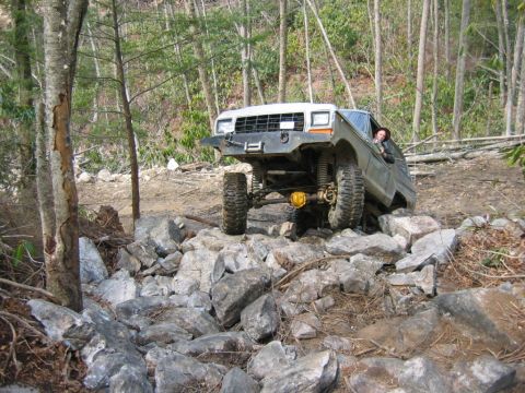 1992 Ford Mustang - An off-road vehicle is shown traversing a challenging rocky terrain in a wooded area.