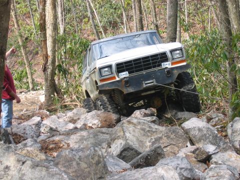 1992 Ford Mustang - A white off-road vehicle navigates a challenging rocky terrain in a wooded area.