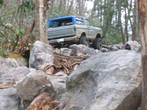 1992 Ford Mustang - Ford Bronco navigating a challenging rocky trail in a wooded area.