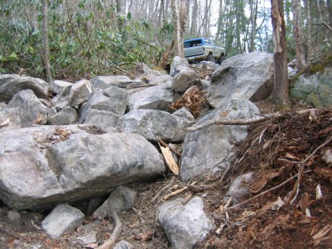 1992 Ford Mustang - A truck is shown driving over a challenging rocky path in a forest.