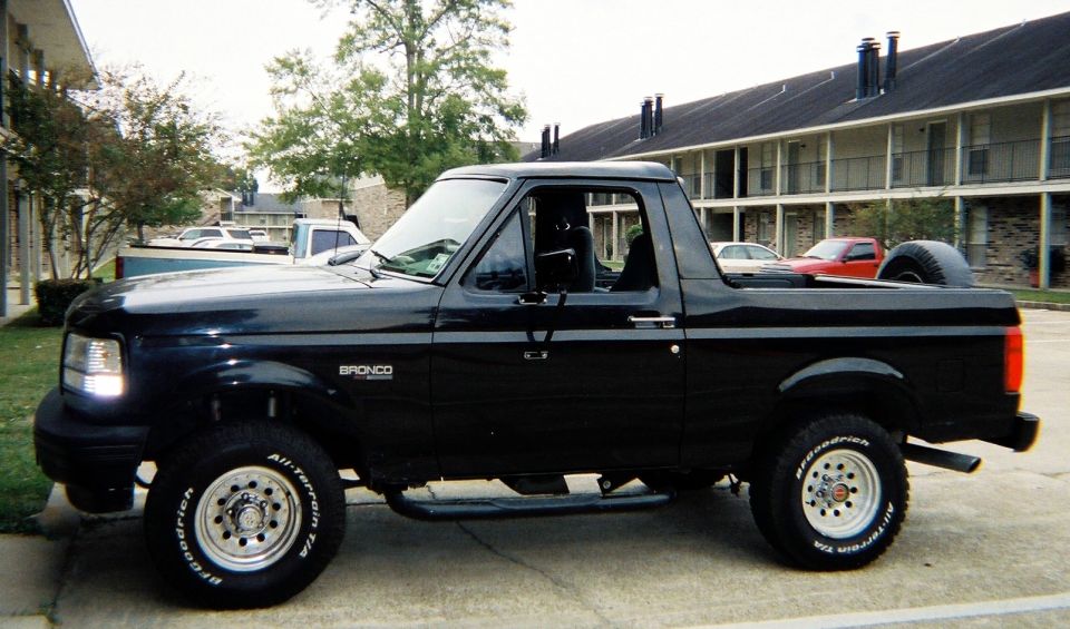 Black lifted Ford Bronco SUV with top removed parked by apartments