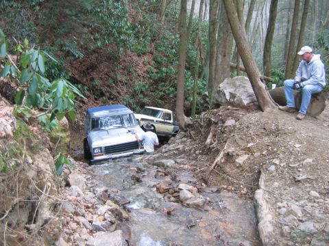 1992 Ford Mustang - Off-road vehicles attempt to navigate a challenging stream crossing in a wooded area.