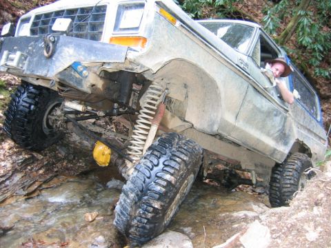 1992 Ford Mustang - This heavily modified off-road vehicle is shown tackling a challenging stream crossing with its tires and suspension clearly visible.