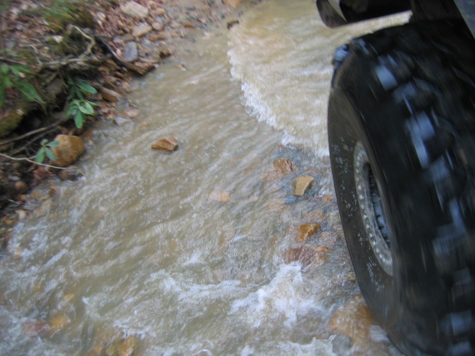 Tire of an off-road vehicle splashing through a shallow stream on a dirt path