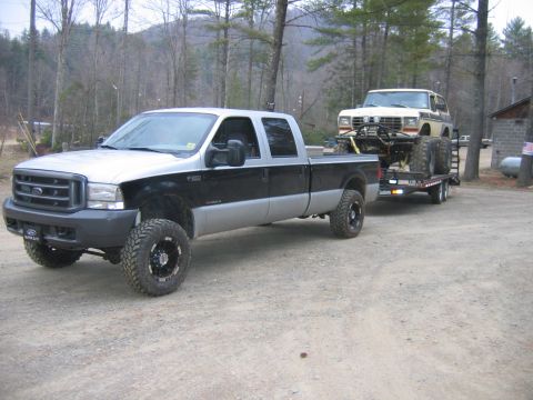 1992 Ford Mustang - A Ford F-350 tows a heavily modified Ford Bronco on a trailer through a wooded area.