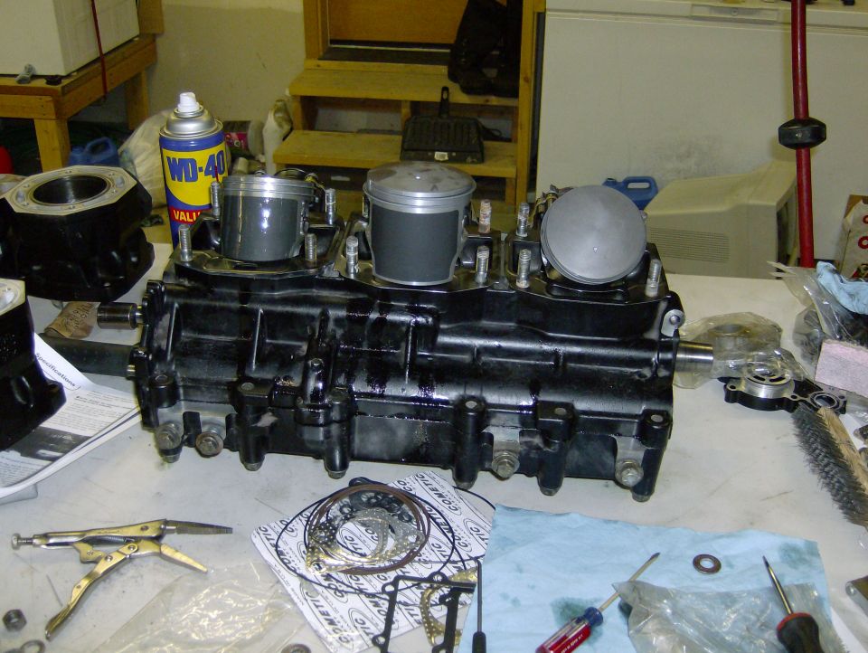 Black engine block with three pistons, on a workbench with tools and parts