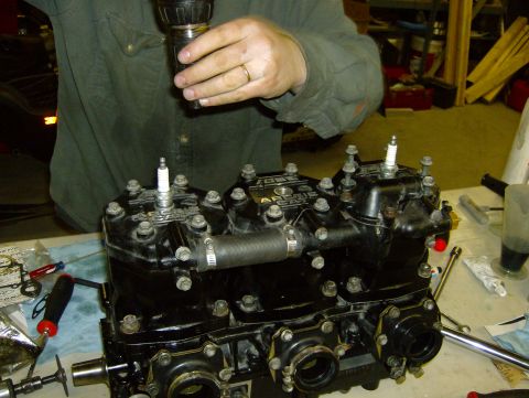 1982 Chevrolet C/K Pickup - Close-up of a black engine part, possibly from a snowmobile, with spark plugs and a hose attached. Tools are visible on the workbench.