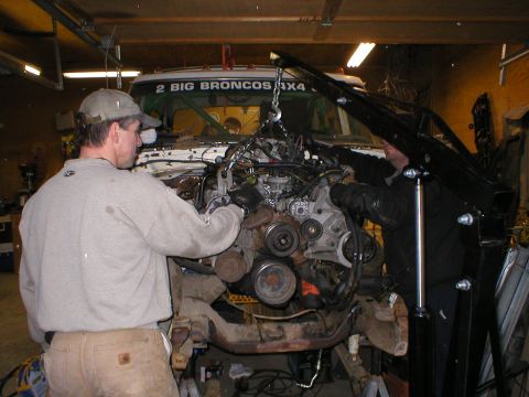 1978 Ford Bronco - Mechanics are using a crane to lift an engine out of a vehicle in a garage setting.