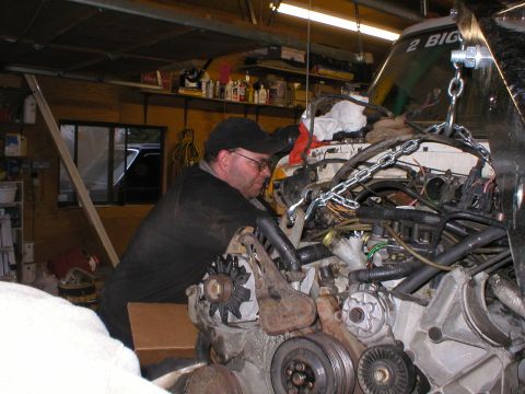 1978 Ford Bronco - Mechanic works on a complex engine assembly, possibly during an EFI swap, with a chain hoist overhead.