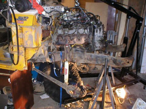 1978 Ford Bronco - Engine and chassis assembly undergoing work, with a mechanic positioned below for repairs or modifications.