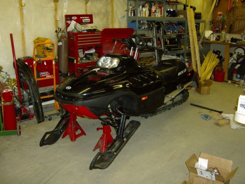 1982 Chevrolet C/K Pickup - A black Arctic Cat snowmobile is elevated on jack stands inside a cluttered garage.