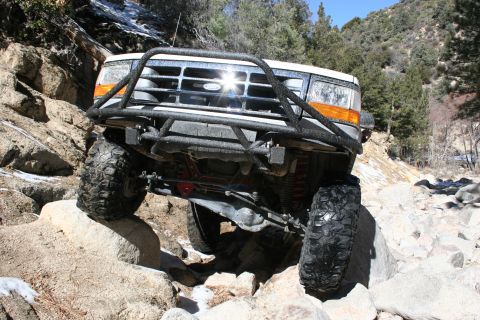 1996 Ford Bronco - A white Ford Bronco with a black bull bar and off-road tires is shown on a rocky trail.