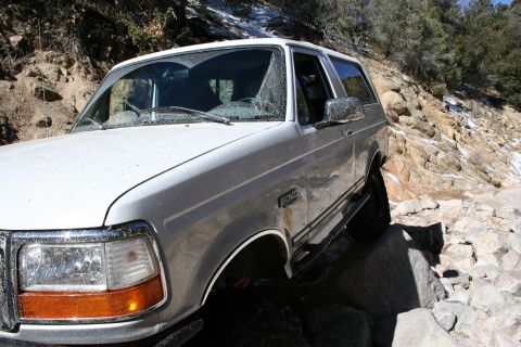 1996 Ford Bronco - White 1996 Ford Bronco tackling a difficult off-road path with large rocks and some snow.