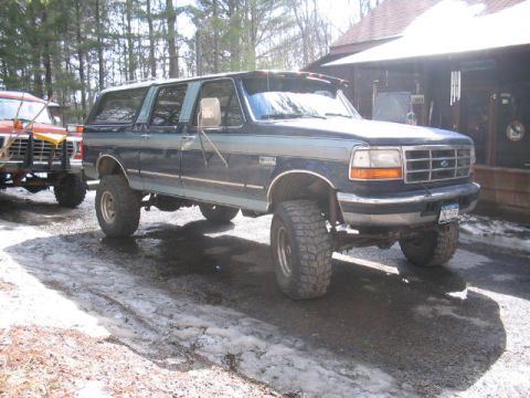 1979 Ford Bronco - A lifted Ford Bronco with a two-tone paint scheme sits parked on a gravel surface next to another vehicle.