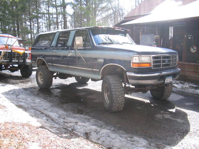 Dark blue lifted Ford crew cab pickup with topper on gravel driveway