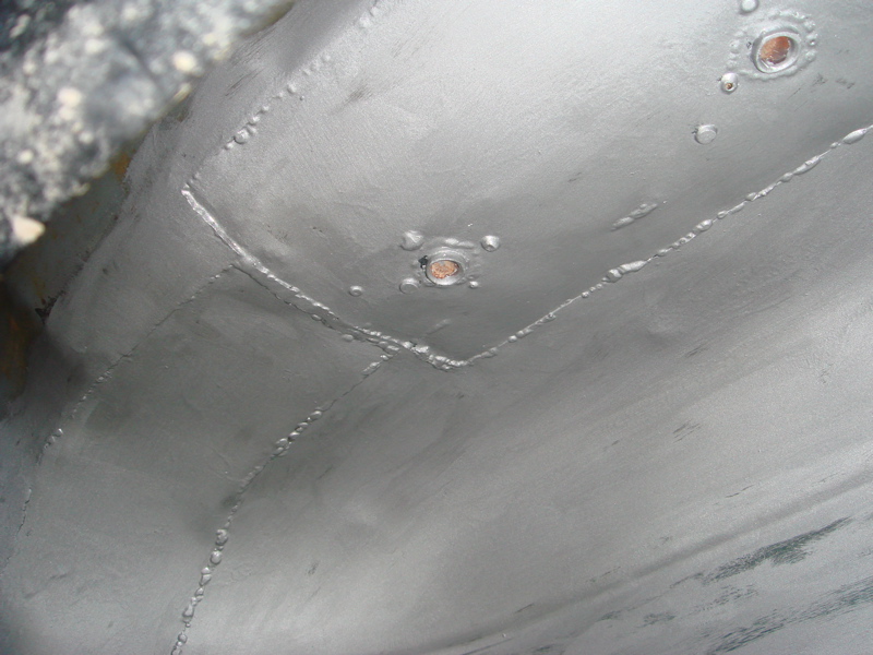 Close-up of a vehicle's underbody showing welded seams and rivets, painted silver