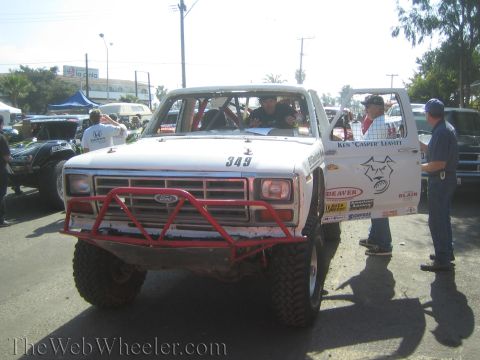 1990 Ford Bronco - Front view of white Ford race truck 349 with a red tube bumper and open driver door as men stand alongside on pavement.