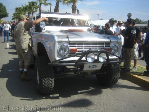 1990 Ford Bronco - silver early Ford Bronco with a roof light bar and tube bumper is surrounded by spectators along a street event.