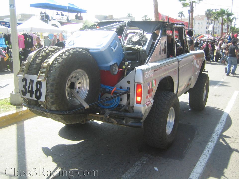 Rear three-quarter view of silver Ford Bronco race truck 348 with spare tire and cooling