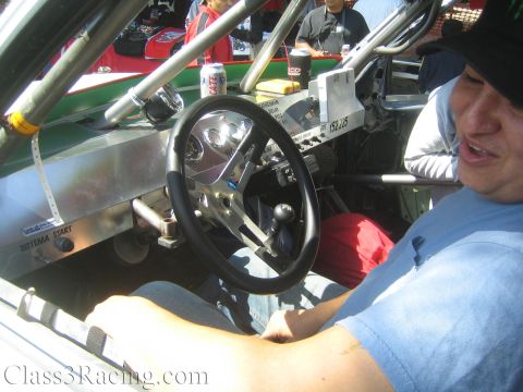 1990 Ford Bronco - man sits at the steering wheel inside an off-road race car with an aluminum dash, roll cage and Sistema Start label.