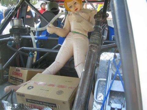 1990 Ford Bronco - inflatable doll is propped on a cardboard box inside the diamond-plate, tube-frame cockpit of a race vehicle as a humorous touch.