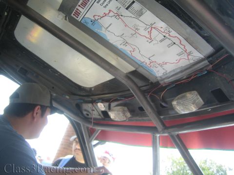 1990 Ford Bronco - printed race course map is fixed to the roll-cage headliner above a dome light inside a race vehicle, with a man in a cap seated below.