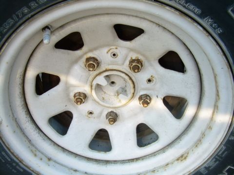 1988 Ford Bronco - Close-up of a white steel wheel with visible lug nuts and tire sidewall markings.