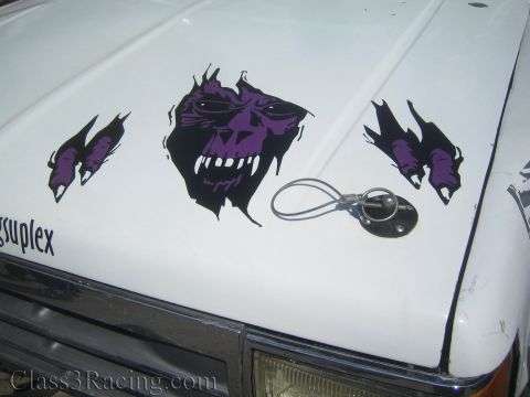 1990 Ford Bronco - Purple skull and torn-metal graphics decorate the white hood of a race truck near a wire hood pin and a single round headlight.
