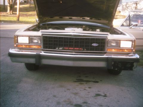 1985 Ford Crown Victoria LTD - The front end of a Ford Crown Victoria is shown with its hood up, parked next to another vehicle.
