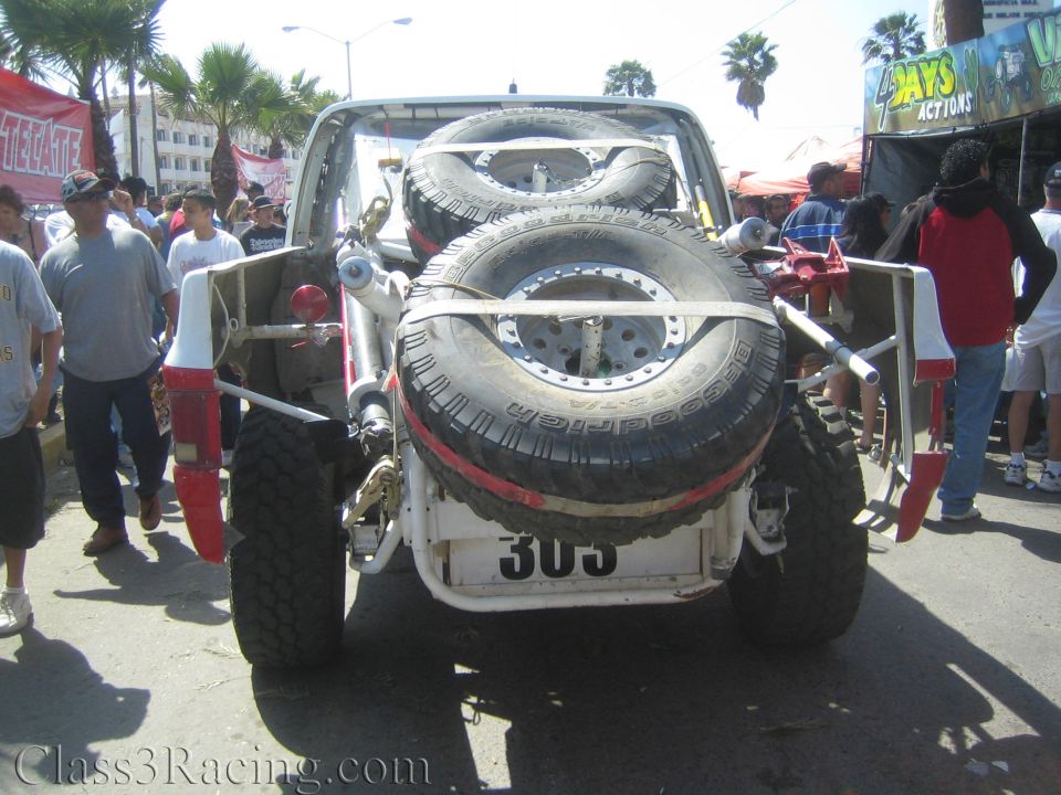 Rear view of white number 303 race truck with spare tires in a crowd