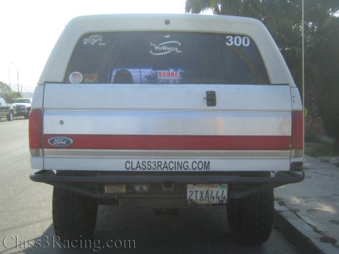 1990 Ford Bronco - Rear view of a white lifted Ford SUV marked 300 with a red bodyside stripe and California plate 2TXA444.