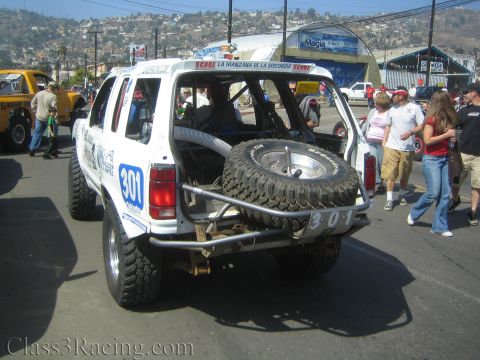 1990 Ford Bronco - Rear of a white off-road SUV marked 301 with a spare tire on a tubular bumper, surrounded by a crowd of people.
