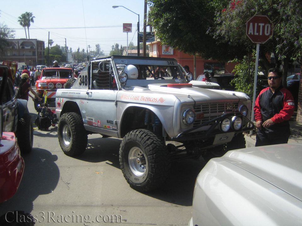 Silver early Ford Bronco off-road truck numbered 348 parked on a street by ALTO sign