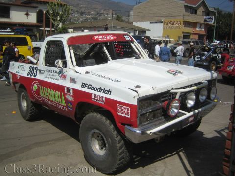 1990 Ford Bronco - Front three-quarter of a red and white off-road race truck marked 303 with California Tomatoes and BFGoodrich decals on a street.