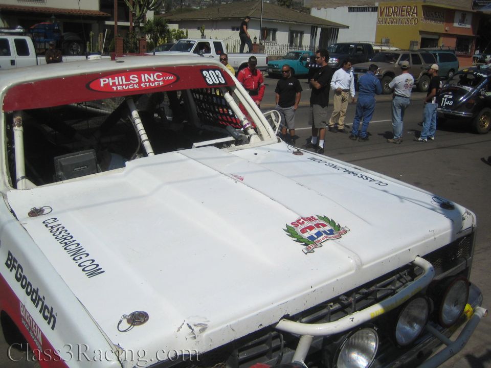Hood of white and red race truck 303 with Class3Racing.com decal and crew standing nearby