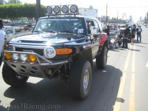 1990 Ford Bronco - Front quarter of a black Toyota FJ Cruiser race truck marked 302 with a roof light bar and donahoeracing.com lettering.