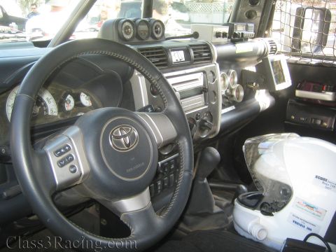 1990 Ford Bronco - Interior of a Toyota FJ Cruiser showing the steering wheel with Toyota logo, dash gauges, a CB radio and a white helmet.