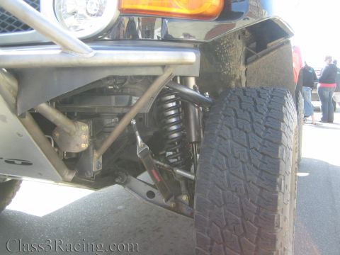 1990 Ford Bronco - Close-up of the front suspension on an off-road vehicle with a coilover shock, tube bumper, amber turn signal and oversized all-terrain tir…