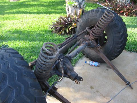 1974 Ford F-100 - Disassembled front axle and suspension parts are laid out on the ground next to a grassy area.