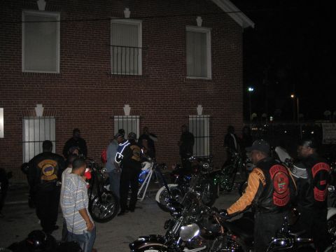 1986 Ford Bronco - A group of people and motorcycles are gathered outside a brick building at night.