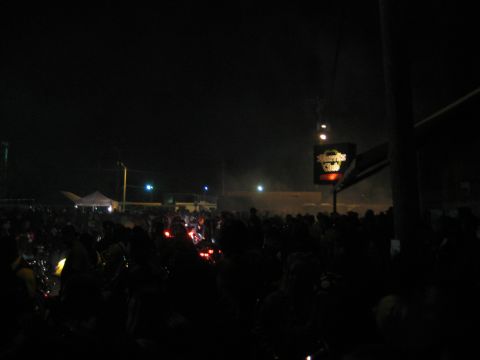 1986 Ford Bronco - A crowd of people are gathered at night under a lit sign for a motorcycle club.