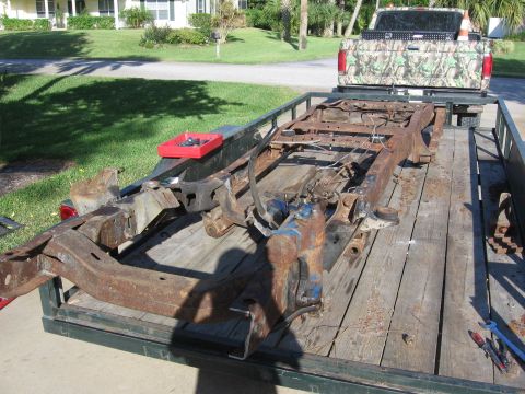 1974 Ford F-100 - A heavily rusted truck frame is transported on a trailer behind a pickup truck.