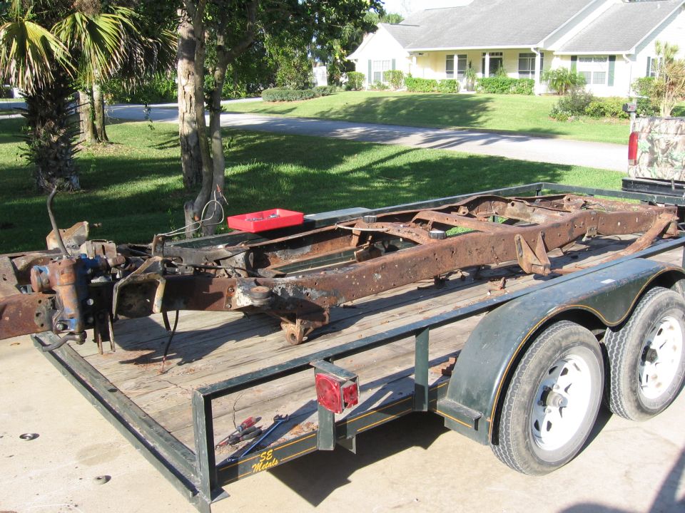 rusted truck frame on a trailer, parked in front of a house