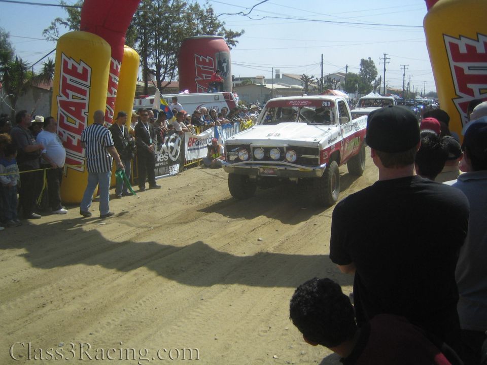 White vintage pickup race truck approaching Tecate arch in dusty crowd