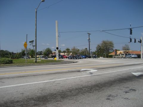 1986 Ford Bronco - Motorcycles wait at an intersection on a sunny day, with cars and buildings visible.