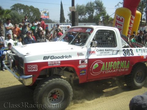 1990 Ford Bronco - Side view of a red-and-white off-road race truck #303 lettered California Tomatoes with driver names Chris Raffo and Jeff Dolan.