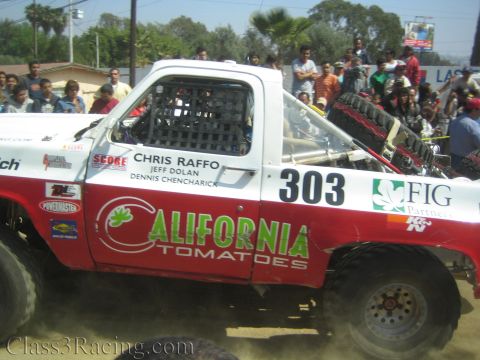 1990 Ford Bronco - white vintage pickup-style off-road race truck with BFGoodrich livery and round driving lights moves along the dusty course.